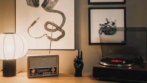 Ein Holztisch mit einem Vintage-Radio, Kopfhörern und gerahmten Bildern an der Wand.