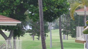 A view of a golf course with trees and a building with a balcony. - 2-bedroom ocean golf course condo in beautiful Kailua-Kona w/ cool ocean breezes (Kailua-Kona)