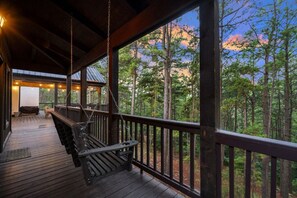 Una terraza de madera con un columpio, un espacio de estar cubierto y vistas a un bosque.