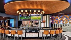 A bar area with a circular bar, multiple screens, and a colorful geometric wall design.