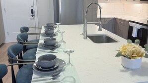A modern kitchen with a central island, stainless steel appliances, and a dining area with chairs and table set for six.