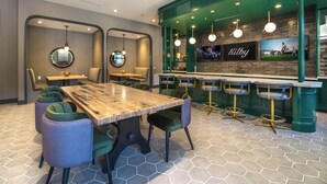 A modern bar area with a wooden table, green upholstered chairs, and a bar counter with stools.