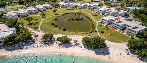 An aerial view of a resort with multiple buildings, a central pond, and a beach area.