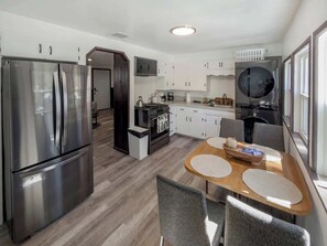 A modern kitchen with stainless steel appliances, a dining area with a round table, and a view of the living area. - Eagle Point Walk to Lake & Hot Tub (Big Bear Lake)