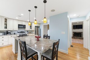 Una cocina moderna con armarios blancos, una isla de granito e iluminación colgante.
