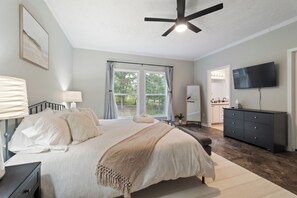 Ein Schlafzimmer mit einem Bett, Nachttischen, einem Schminktisch, einem Fernseher und einem Deckenventilator.