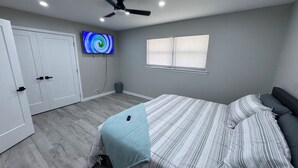 Ein Schlafzimmer mit Bett, Deckenventilator, Fernseher, Fenster und Tür.