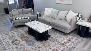 Ein Wohnzimmer mit grauem Sofa, einem gemusterten Teppich und einem Marmortisch.