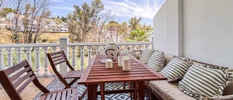 A balcony with a wooden table and chairs, a sofa with striped cushions, and a decorative vase.
