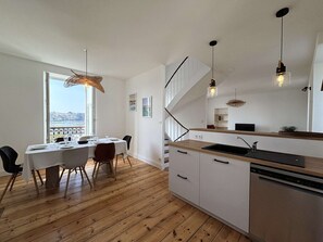 Eine moderne Küche mit Holzboden, weißen Schränken, einem eingebauten Geschirrspüler und einem Essbereich mit Tisch und Stühlen.