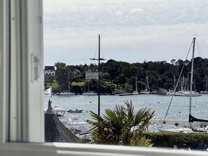 Uma marina com barcos, uma casa e uma colina arborizada ao fundo.