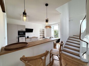 Eine moderne Küche mit einer Holztheke, ein Essbereich mit Korbstühlen und eine Treppe mit Aussicht.