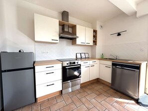 A compact kitchen with white cabinets, a stainless steel refrigerator, oven, dishwasher, and a wooden countertop. - Bénodet – Charming apartment at the port, facing the sea (BENODET)
