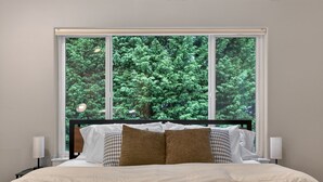Ein Schlafzimmer mit großem Fenster, einem Bett mit weißem und gemustertem Kopfkissen und Nachttischlampen.