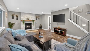 Ein modernes Wohnzimmer mit Kamin, Flachbildfernseher, einer Wendeltreppe und einem Bücherregal.