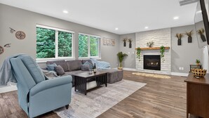 Ein modernes Wohnzimmer mit Sofa, Couchtisch, Kamin und großen Fenstern.