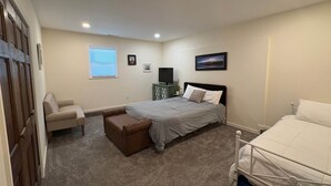 Un dormitorio con cama, una silla, escritorio, televisor y ventana.
