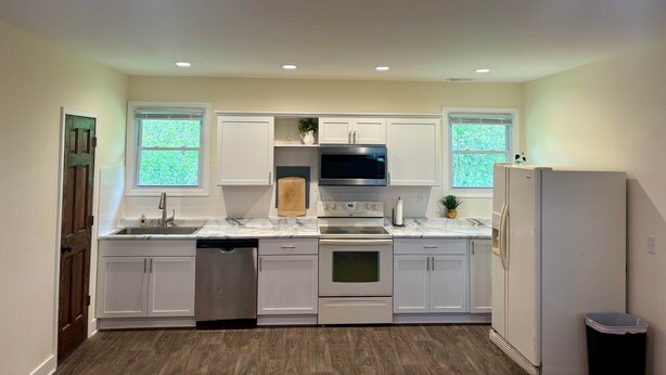 Una cocina moderna con armarios blancos, un lavavajillas de acero inoxidable, un microondas integrado y un refrigerador.