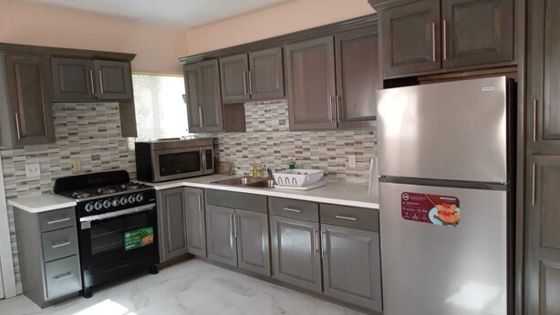 A kitchen with grey cabinets, a stainless steel refrigerator, a microwave, and a stove. - Hilltop overlooking the stunning beach at Love Hill, Central Andros Island. (Andros Island)