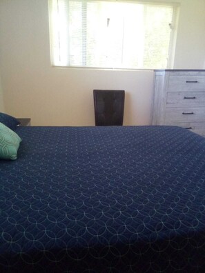 Une chambre à coucher comprenant un lit, une chaise, une commode et une fenêtre avec des stores.