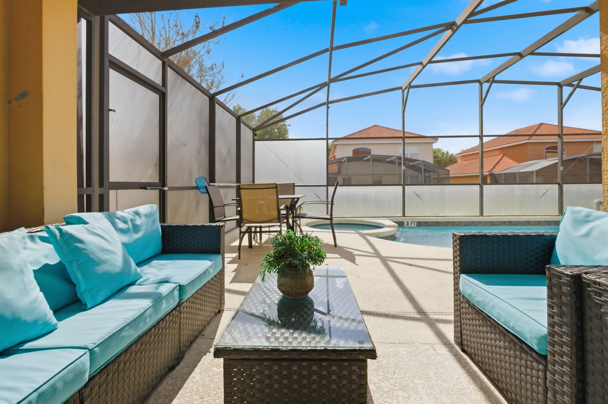 A covered outdoor area with a pool, wicker furniture, and a glass table with a plant.