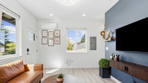 Un salon moderne avec un canapé, une table basse ronde, un téléviseur fixé au mur et des certificats encadrés accrochés au mur.