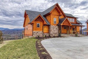 A large wooden house with a stone foundation, a driveway, and a view of mountains. - Sweet Mimosa Lodge | Indoor Pool, Hot Tub, Views (Sevierville)