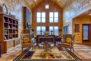 A log cabin interior with a fireplace, two leather armchairs, a coffee table, and a bookshelf. - Sweet Mimosa Lodge | Indoor Pool, Hot Tub, Views (Sevierville)