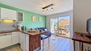 A compact kitchen with a wooden island, a dining area with a blue sofa, and a sliding glass door leading to an outdoor patio. - Carnac - 2-room apartment - 30m² (CARNAC)