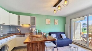 A compact kitchen with a wooden island, a built-in washing machine, and a dining area with a blue sofa and a small table. - Carnac - 2-room apartment - 30m² (CARNAC)