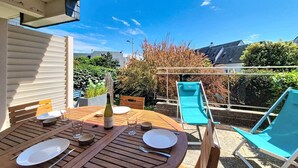 A wooden table set for two with plates, cutlery, and a bottle, surrounded by chairs and a view of a garden. - Carnac - 2-room apartment - 30m² (CARNAC)