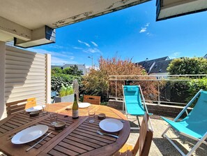 Ein Holztisch für zwei Personen gedeckt mit Tellern, Besteck und einer Flasche, umgeben von Stühlen und Blick auf einen Garten.