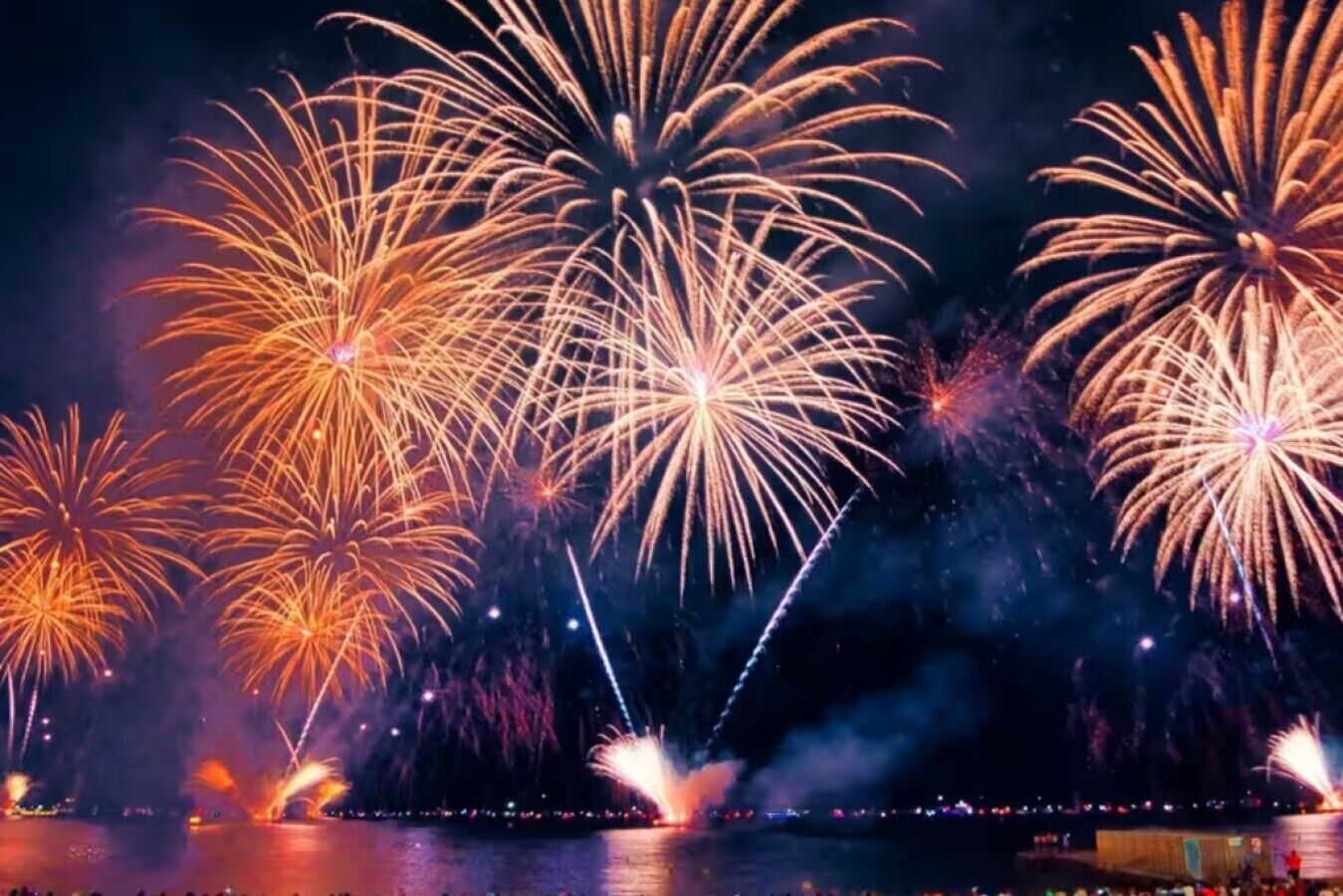 A nighttime view of fireworks over a body of water with a distant cityscape.