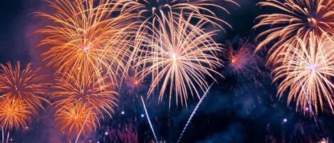 A nighttime view of fireworks over a body of water with a distant cityscape.