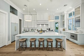 A spacious kitchen with a large island, white cabinetry, and bar stools.
