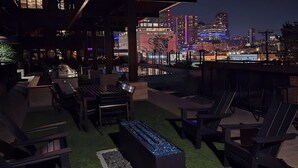 An outdoor seating area with Adirondack chairs and a fire feature, overlooking a city skyline at night. - The Trendy Den  Music & Nightlife Nearby (Dallas)