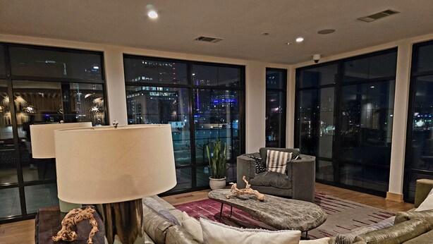 A modern living room with a large window, a sofa, a coffee table, and a lamp. - The Trendy Den  Music & Nightlife Nearby (Dallas)