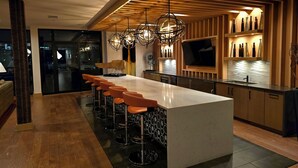 A modern kitchen with a large island, bar stools, pendant lighting, and a TV mounted above the counter. - The Trendy Den  Music & Nightlife Nearby (Dallas)