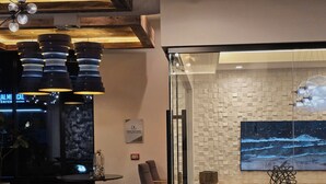 A modern interior with a glass partition, a desk, chairs, a large wall-mounted TV, and a ceiling with exposed beams and pendant lighting. - The Trendy Den  Music & Nightlife Nearby (Dallas)