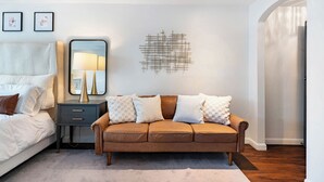 Ein Schlafzimmer mit einem Bett, einem Nachttisch, einer Lampe und einem braunen Sofa mit gemusterten Kissen.
