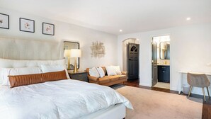 Ein Schlafzimmer mit einem großen Bett, einem Schlafsofa, einem Schreibtisch und einem durchgegangenen Tür sichtbaren Badezimmer.