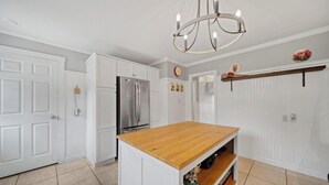 A kitchen with white cabinetry, a stainless steel refrigerator, a wooden island, and a chandelier.