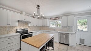 A modern kitchen with white cabinetry, a wooden countertop, a built-in oven, and a stainless steel dishwasher.