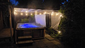 A hot tub with a wooden deck and steps, surrounded by a covered area with string lights.