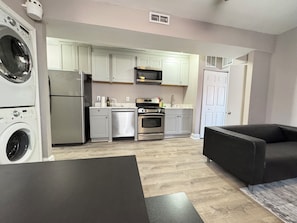 A compact kitchen with a washing machine, microwave, oven, and sink. There is a dark-colored sofa and a table in the living area.