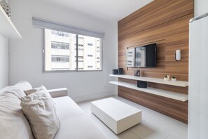 Un salon moderne avec un canapé, une table basse, un téléviseur fixé à un mur en bois et une fenêtre donnant sur un immeuble.