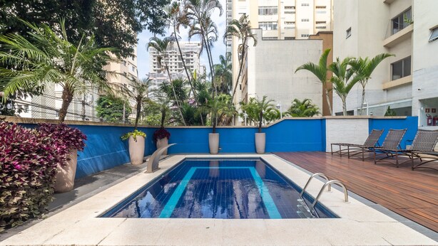 Ein Pool mit blauem Wasserspiel, umgeben von Holzterrasse und Kübelpflanzen.