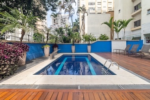 Ein Pool mit blauem Wasserspiel, umgeben von Holzterrasse und Kübelpflanzen.