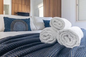 A neatly made bed with rolled white towels, a dark blue patterned blanket, and a blue pillow with a concentric circle design. - OF1799_902 (São Paulo)