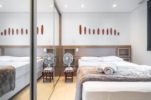Ein Hotelzimmer mit zwei Betten, einem Spiegel, einem Ventilator und Wandbildern.
